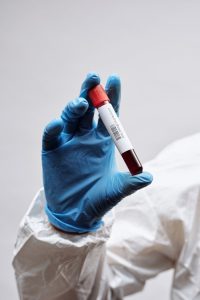 Close-up of a gloved hand holding a blood sample in a test tube against a white background.